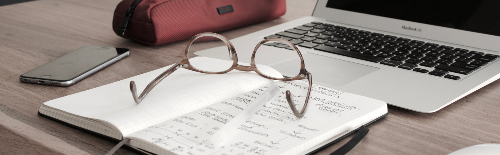 Notebook with a pair of glasses on top. Near a laptop computer.